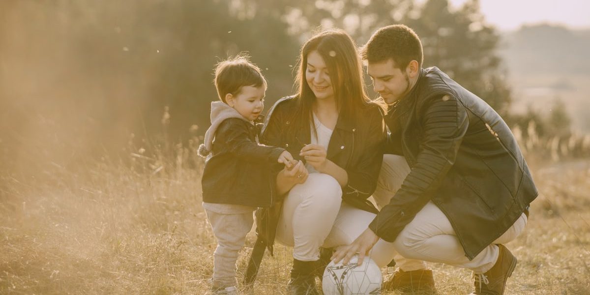 A cheerful family bonding outdoors with a soccer ball, enjoying a sunny day in the grass.