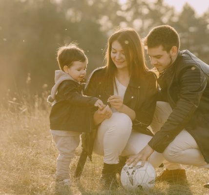A cheerful family bonding outdoors with a soccer ball, enjoying a sunny day in the grass.